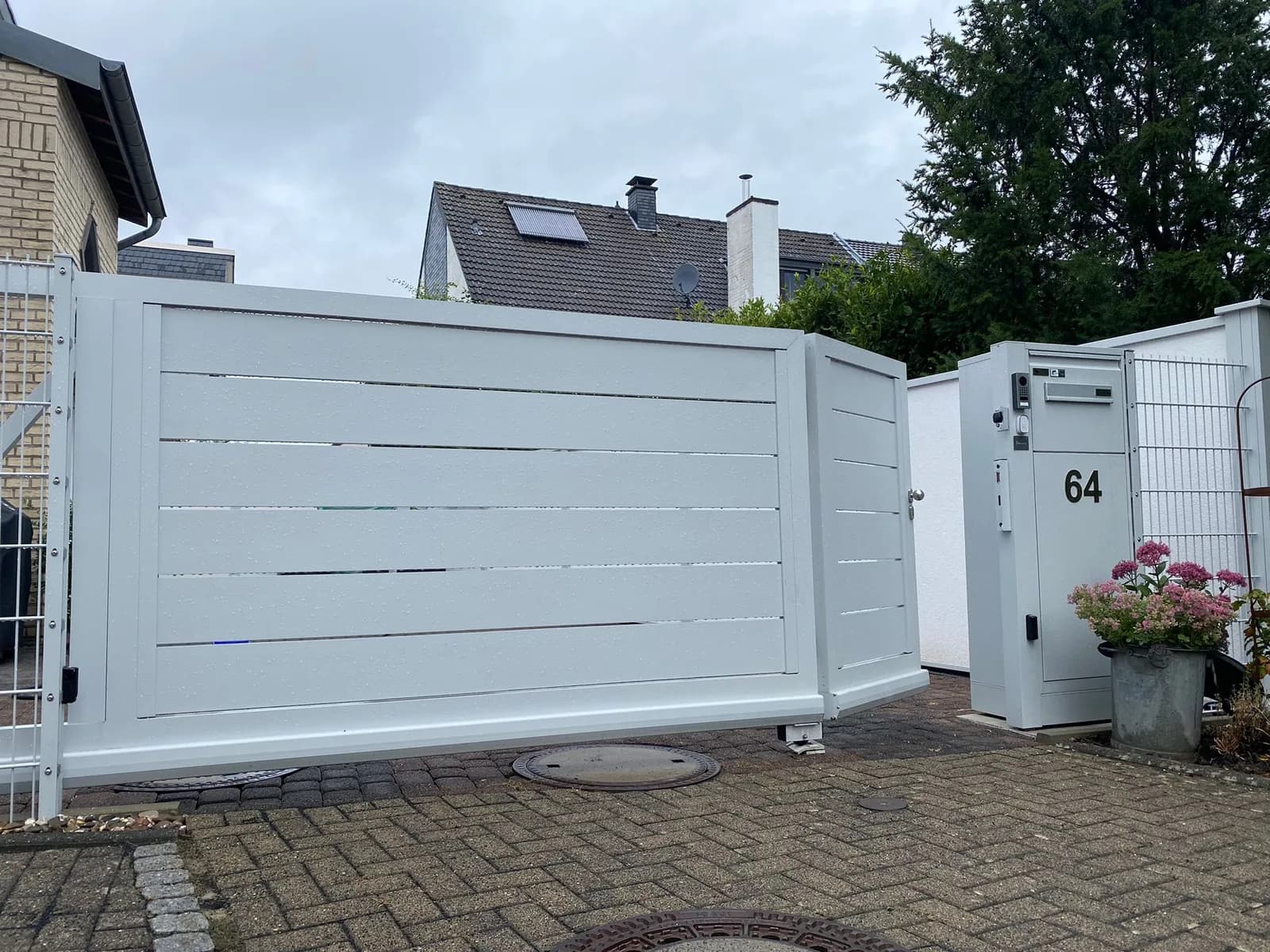 Weißes Tor mit waagerechten Elementen an einem hellen Haus.