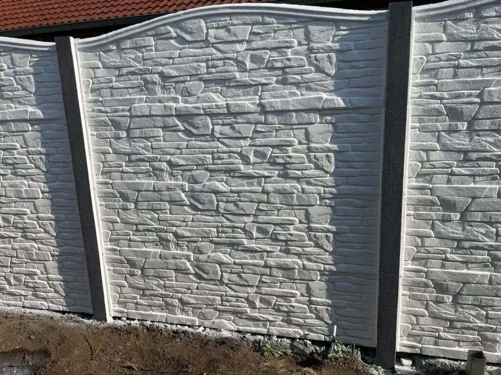 Nahaufnahme grauer Betonzaunfelder mit Steinrelief zwischen senkrechten Pfosten.