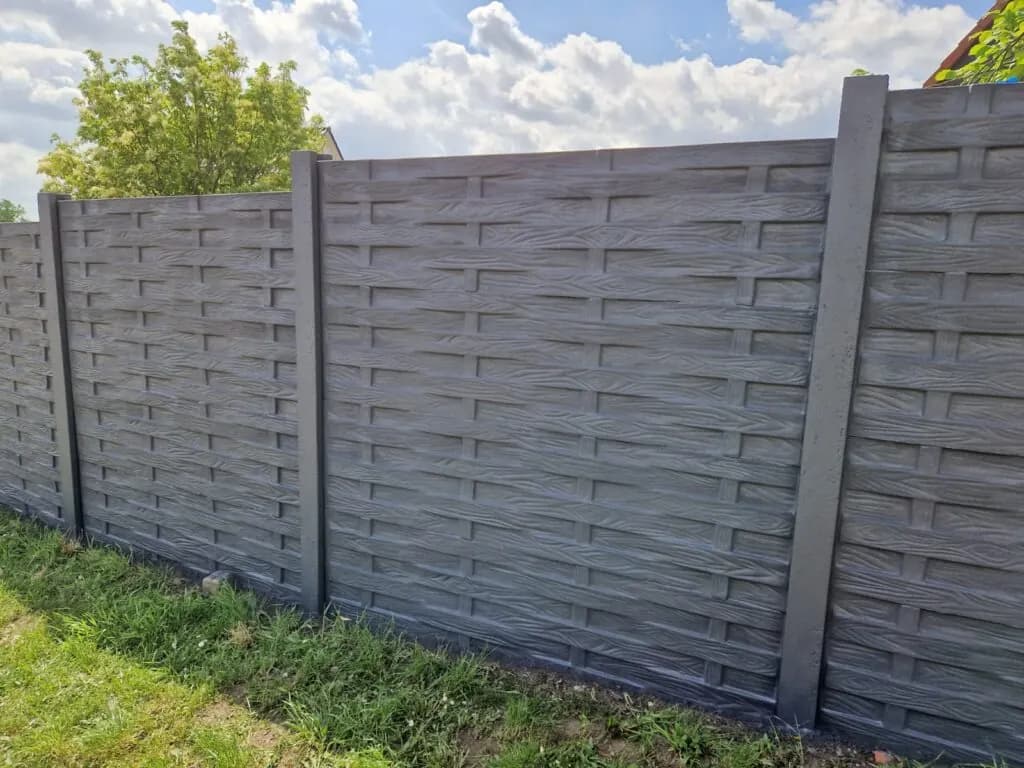 Graue Betonzaunfelder mit waagerechter Flechtstruktur zwischen geraden Pfosten im Garten.