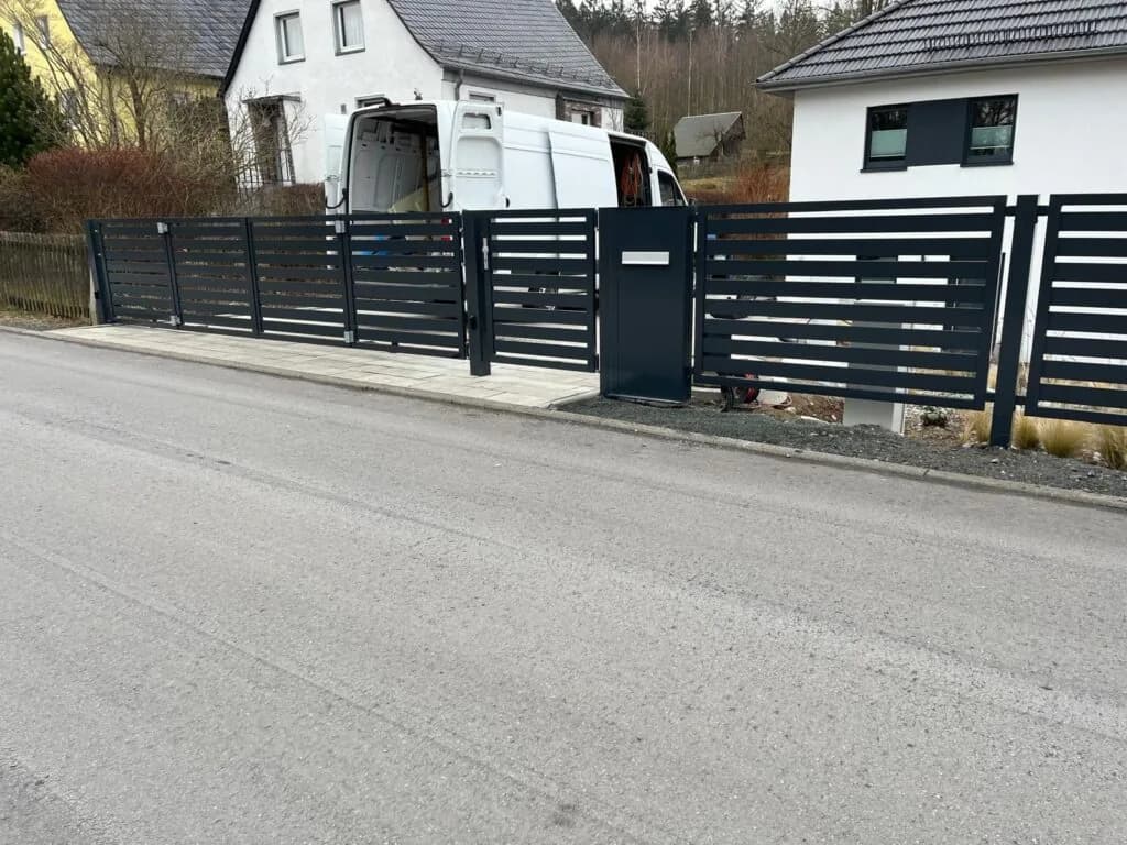 Ausgeführte Zaunanlage von MMS Stark mit waagerechten Streben, Durchgang und Tor an einer Straße.