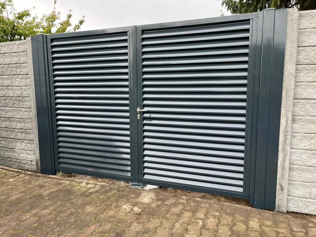 Dunkles zweiflügeliges Tor mit waagerechten Lamellen zwischen hellen Betonmauern.