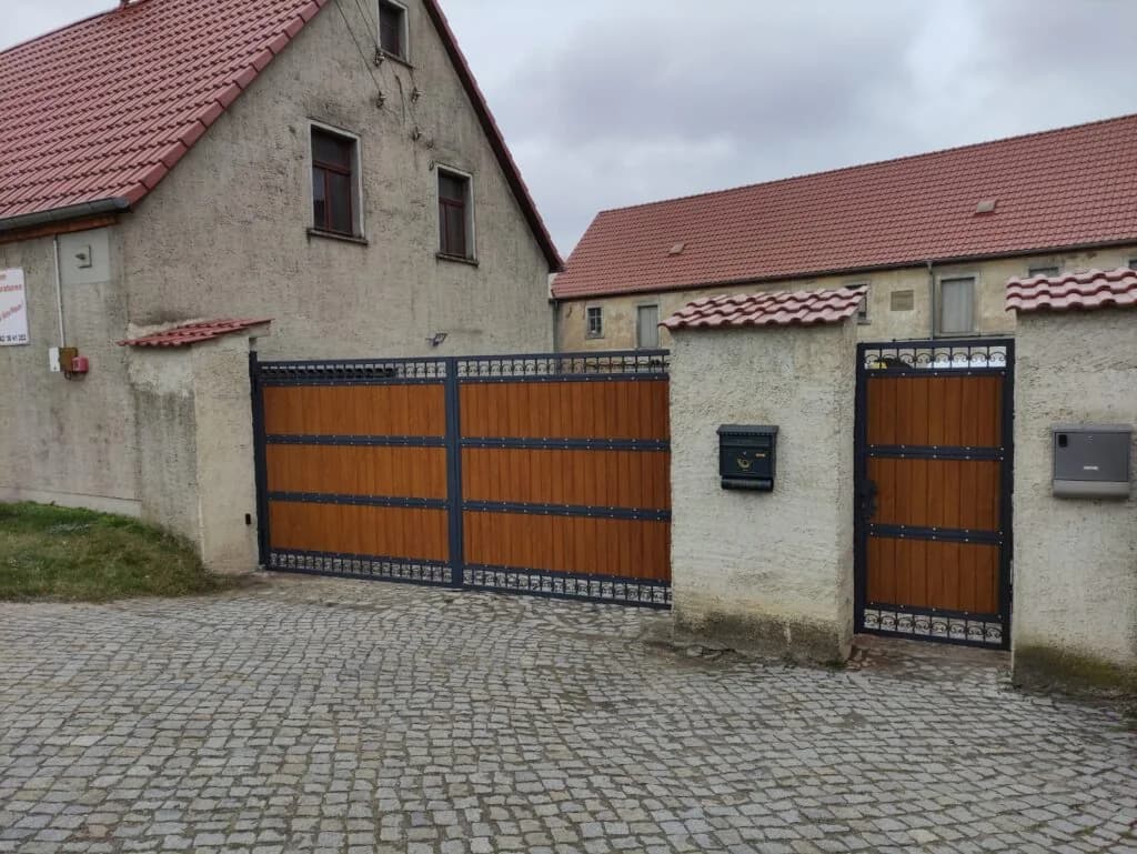Zweiflügeliges Tor mit braunen Füllungen und dunklem Zierrahmen neben einer separaten Gehtür.